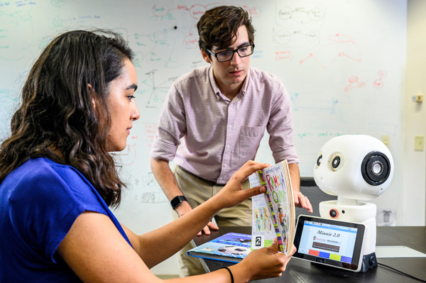 Two students work with a robot on teaching children to read. 