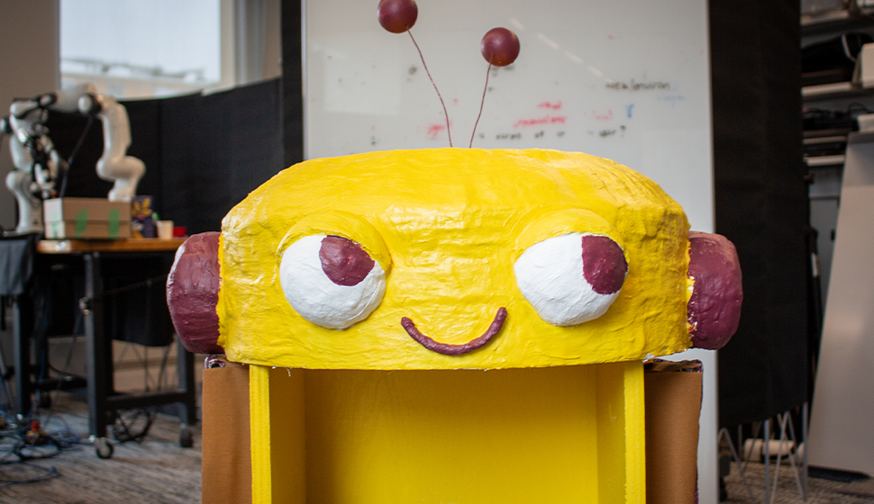"Oimo-don," a cheeky yellow robot prototype designed by Amy Koike, smiles at the camera.
