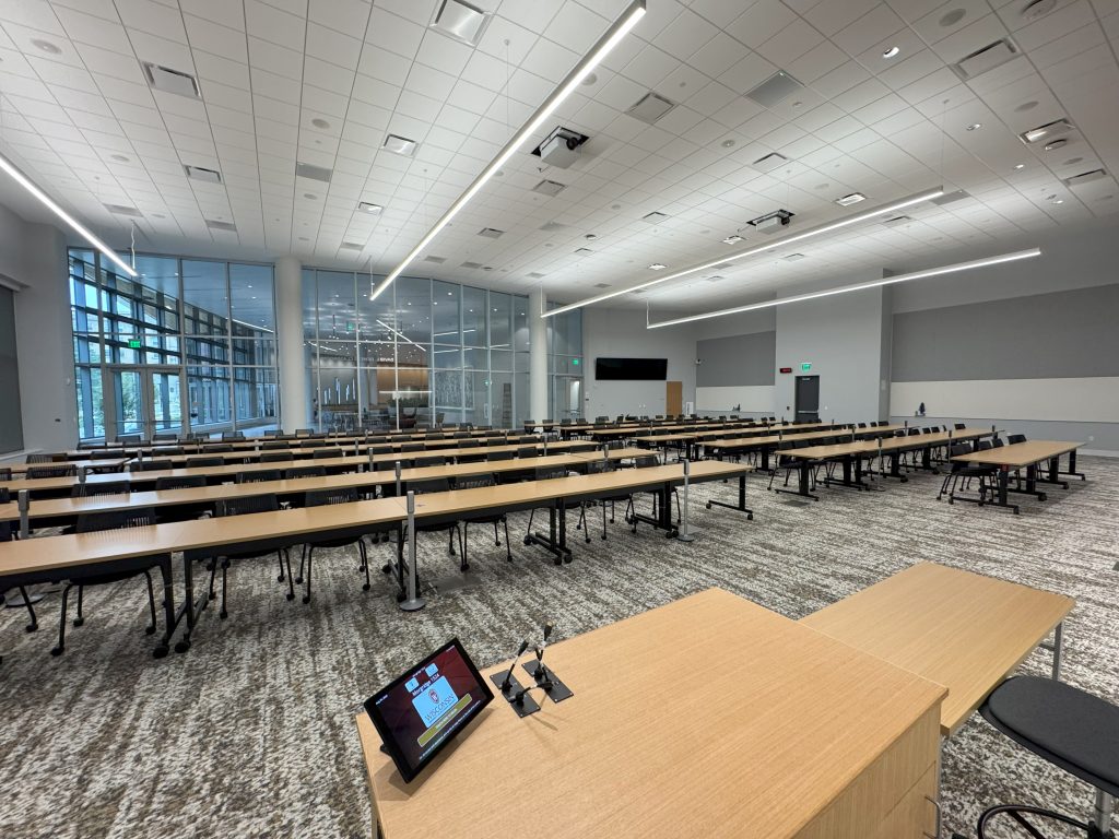 An empty classroom with tables and chairs and full-length windows at the back.