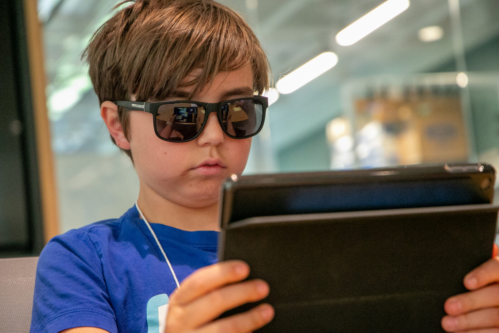 A middle schooler in sunglasses looks at a tablet. 