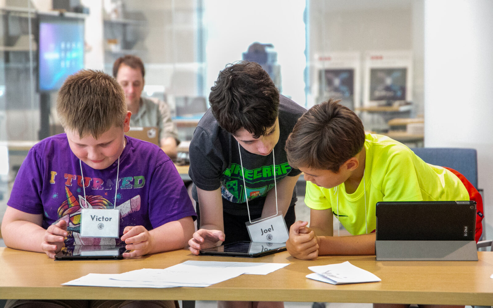 Three students lean over a tablet, working together. 