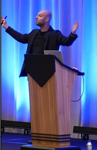 Aws speaks to an audience with arms raised.